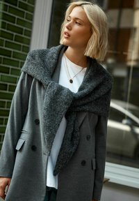 Gray double-breasted coat with a large, textured shawl collar. Underneath is a white t-shirt, and a delicate gold necklace is visible.