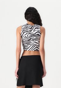 Cropped tank top in black and white zebra print, with a round neckline and sleeveless design, paired with a high-waisted black skirt.