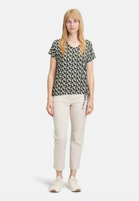 Schwarz-weiß gemusterte kurzärmlige Bluse mit V-Ausschnitt und Bindedetail an der Seite, kombiniert mit hellbeigen, schmalen Hosen und weißen Sneakers.