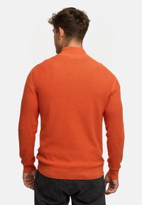 Orange strikket sweater med høj krave og ribbede manchetter. Har struktureret stof og et tætsiddende design, vist fra ryggen.