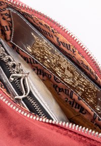 Borsa a pochette rossa in suede con zip argentata, dotata di una fodera interna a fantasia in tonalità di arancione e nero, e un dettaglio in ciondolo metallico.