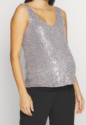 Kvinde iført ærmeløs sølvglimmer-top med V-hals og sorte bukser, vist fra nakke til hofter mod en ensfarvet baggrund.