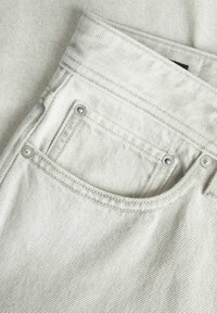 Svetlo sivi jeans material z zadnjim žepom, okrašenim s srebrnimi kovinskimi nitmi in detajli šivanja, ki ponuja teksturiran, reberast vzorec.