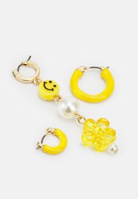 Brincos em forma de argola amarelos com um encanto de sorriso, pérola branca e um detalhe floral. Apresentam uma textura brilhante e acabamentos em metal dourado.