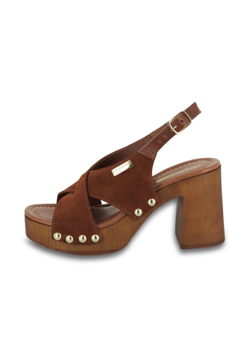 Sandal en suède marron à plateforme avec des bandes croisées, des clous dorés sur le devant et un talon en bois marron épais. Sangle réglable avec boucle.