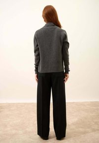 Szary wełniany sweter z wysokim kołnierzem zestawiony z czarnymi szerokimi spodniami. Tekstura swetra wydaje się miękka i przytulna.