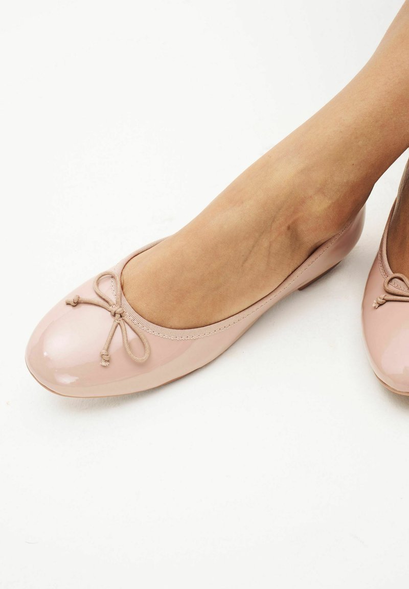 Bailarinas patent rosas con punta redondeada, ribete elástico y un pequeño lazo en la parte delantera. Textura suave y diseño minimalista.