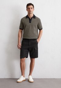 Gestreepte polo met korte mouwen in zwart en beige, gecombineerd met zwarte cargoshorts en witte sneakers, met een kraag met twee knopen en een getailleerde pasvorm.