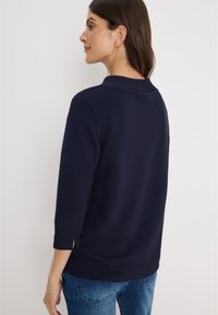 Marinblå, ribbad tröja med trekvartsärmar och sidoslitsar, med en rund halsringning och strukturerad tyg. Avslappnad passform, bärs över jeans.