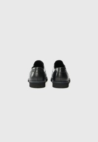 Czarne skórzane buty z gładkim wykończeniem, okrągłym noskiem, niskim, układanym obcasem oraz detalami szwów. Minimalistyczny design, odpowiedni do formalnych stylizacji.