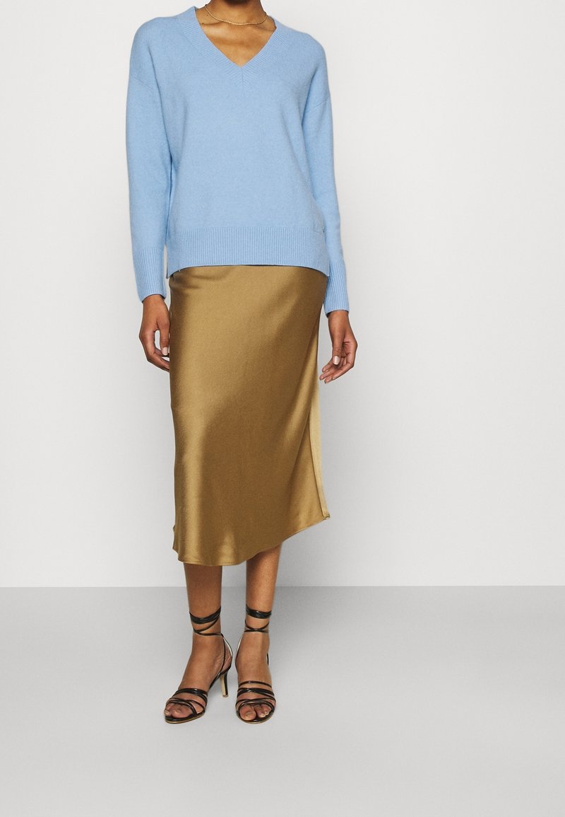 Ljusblå v-ringad tröja med ribbat nederkant, tillsammans med en guldig satin midi kjol med en sidoklyfta. Svarta remsandaler framhäver looken.