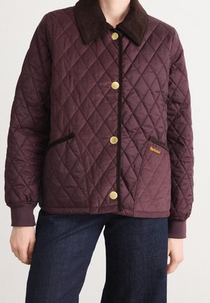 Veste matelassée violet foncé avec boutons dorés, col marron, poches avant inclinées et logo Barbour sur la poche droite, portée avec un jean foncé.