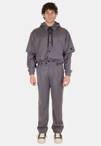 Completo grigio composto da un top con cappuccio, con bottoni e vestibilità rilassata, abbinato a pantaloni sartoriali e sneakers.