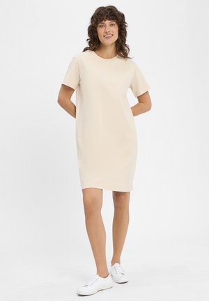 Beige Kurzarm-T-Shirt-Kleid, lockere Passform, Rundhalsausschnitt, knielang, weicher Stoff, kombiniert mit weißen Sneakers.