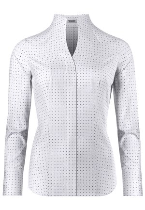 Blouse blanche cintrée à manches longues avec petits pois noirs, col en V et sans boutons ni fermetures visibles.