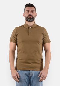 Polo shirt corto marrone a maniche corte con colletto button-down e un logo discreto sul petto. Tessuto liscio e design aderente, abbinato a un denim.