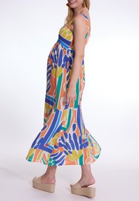 Multikleurige maxi-jurk met een levendig abstract patroon in groen, blauw, oranje en geel, en een gerimpelde bodice. Espadrille sleehaksandalen.