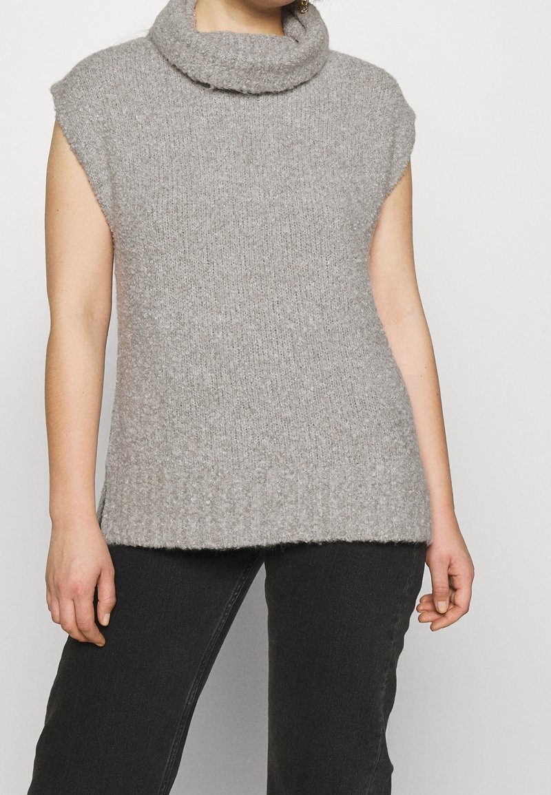 Pull sans manches gris clair avec un col roulé haut. Fabriqué en maille texturée avec une coupe légèrement ample et un ourlet côtelé.