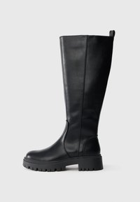 Botă neagră din piele, cu înălțime până la genunchi, cu vârf rotund, talpă din cauciuc rezistentă și detalii discrete la cusături. Dispune de o bandă de prindere în partea de sus pentru o îmbrăcare ușoară.