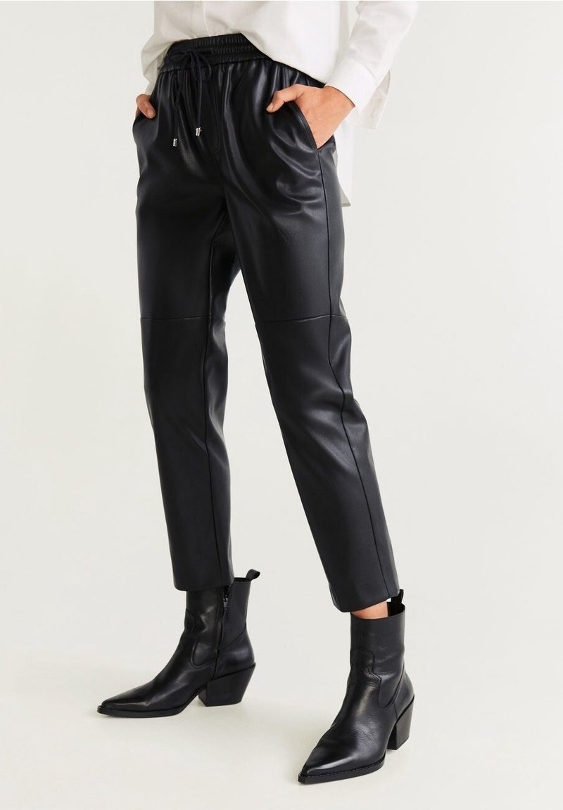 Pantaloni neri in finta pelle con vita regolabile, gambe affusolate e tasche laterali, abbinati a stivaletti neri con punta a punta.