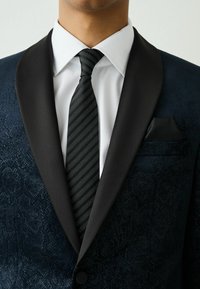 Sacou formal dintr-un material texturat albastru închis, revere din satin negru, cămașă albă și cravată neagră cu dungi. Batistă în buzunar din același material.