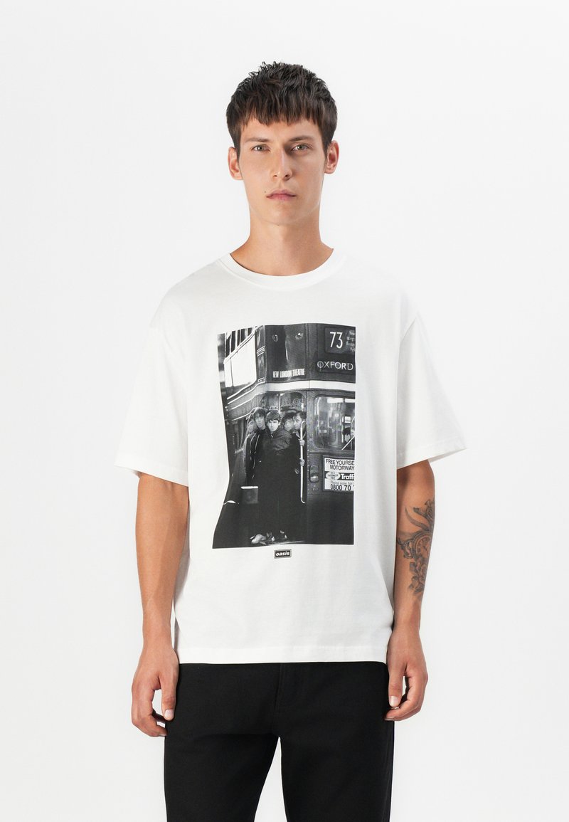 White cotton t-shirt featuring a large black-and-white graphic print of a bus and people. Short sleeves with a relaxed fit, minimalist design.