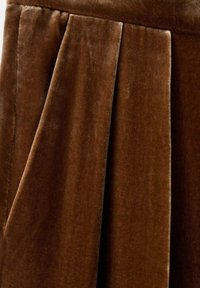 Gonna in velluto marrone con morbida texture e pieghe accentuate, che aggiungono profondità e struttura al design. Superficie liscia e colore ricco.