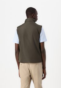 Olive green sleeveless vest with a high collar, smooth texture, and minimalistic design, layered over a light blue short-sleeve shirt.