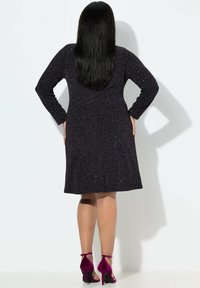 Schwarzes, strukturiertes Kleid knielang mit langen Ärmeln und schwingendem Rock; verfügt über dezente Glitzerpartikel. Getragen mit lila High Heels.