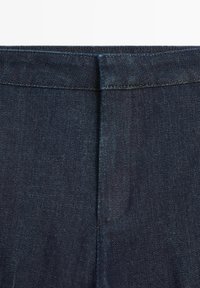Dark denim jeans feature a clean waistband with a smooth texture, vertical seam details, and subtle stitching throughout.
