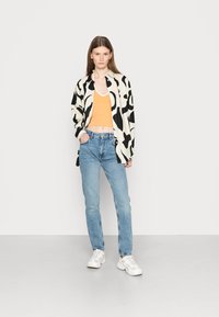 Camisa oversized com padrão preto e branco, top cropped laranja, jeans azul claro e ténis brancos, todos exibidos contra um fundo simples.