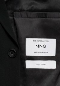 Interiorul de culoare neagră al unui sacou cu un singur nasture negru, etichete marcate "MNG", mărimea EUR-IT 50 și "SUPER SLIM FIT."