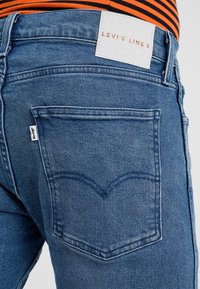 Blå denimjeans med rak passform, med en sydd bakfickdesign och en vit etikett med "Levi's Line 8" i kopparfärgade bokstäver.