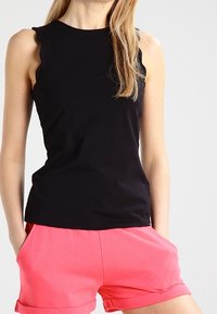 Haut noir sans manches avec un bord en forme d'ondulations aux épaules, associé à un short rose. Le tissu est lisse et le design est décontracté.