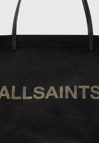 Borsa a tote in canvas nero con un grande logo testurizzato dorato "ALLSAINTS". La borsa è dotata di due manici in pelle nera. Design semplice e spazioso.