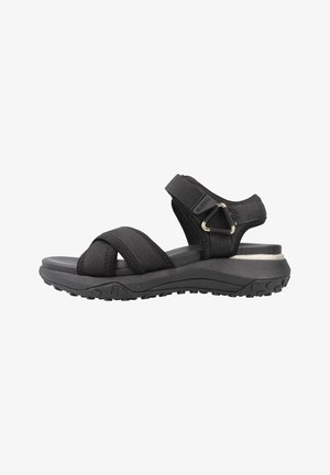 Sandalias negras con múltiples correas elásticas, una plantilla acolchada y una suela de goma texturizada. Presenta un acento metálico decorativo en el talón.