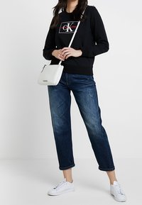 Czarna bluza z logo, niebieskie krótkie dżinsy i białe trampki, w połączeniu z małą białą torebką. Luźny, casualowy strój.