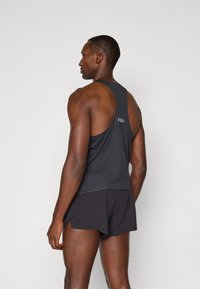 Débardeur de sport noir avec un design dos nageur, associé à un short noir. Le tissu semble léger, avec une texture lisse et un minimum de branding.