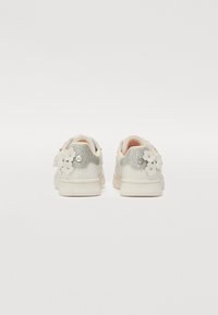 Zapatillas blancas con un talón plateado brillante, adornadas con aplicaciones florales en el costado, que cuentan con una textura suave y suela de goma.