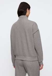Felpa grigia con colletto alto, realizzata in morbido tessuto testurizzato. Vestibilità larga con spalle scese e orlo a costine. Indossata con pantaloni coordinati.