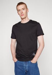 Black cotton t-shirt with a classic crew neckline. Features a small Calvin Klein logo patch on the left side. Short sleeves, regular fit.