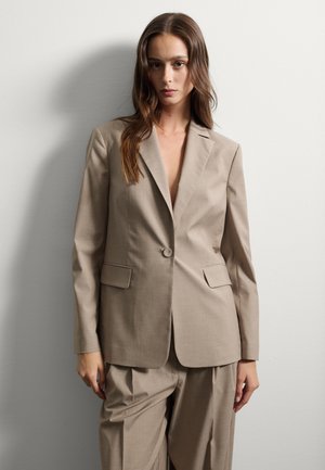 Blazer beige ajusté avec une fermeture à un bouton, revers crantés et deux poches avant, associé à un pantalon ample assorti.