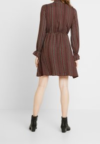 Röd och svart mönstrad klänning med långa ärmar, insvängd midja och utsvängd kjol. Ett par svarta ankelboots fulländar looken.