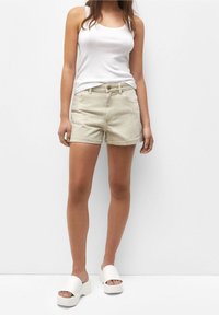 Shorts in denim beige chiaro con orlo sfrangiato, abbinati a una canotta bianca e sandali platform bianchi. L'outfit ha una vestibilità rilassata.