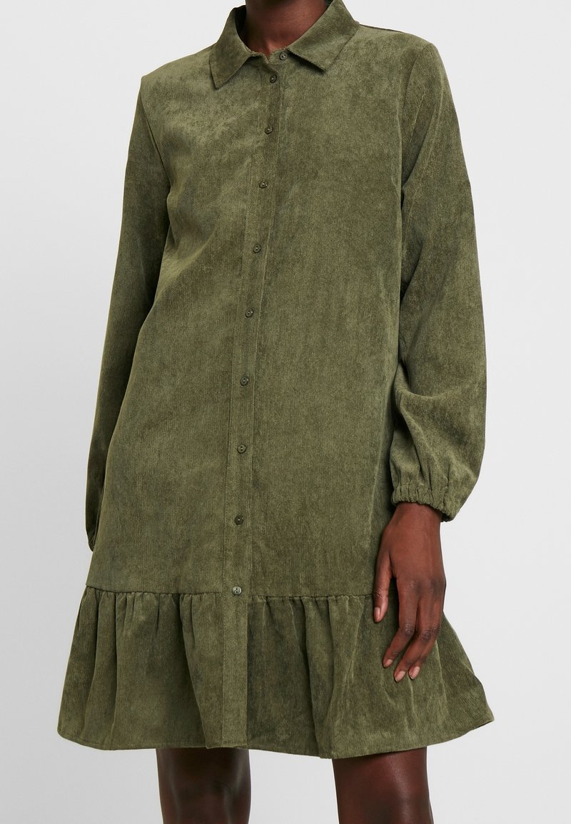 Robe en velours côtelé vert olive avec un col, des manches longues, une fermeture par boutons et un ourlet festonné. Texture lisse, coupe légèrement ample.