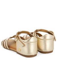 Sandalias metálicas doradas con tira en el tobillo, diseño de punta abierta, material texturizado y suela plana. Detalle de hebilla en el lateral.