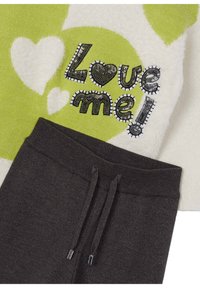 Maglia da pigiama in pile con motivo a cuori verdi e bianchi, con la scritta "Amami!" in paillettes nere; pantaloni jogger in cotone grigio scuro con vita regolabile.