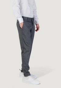 Pantaloni grigi texture con taglio affusolato, dotati di tasche laterali e vita con bottoni, abbinati a sneakers bianche.