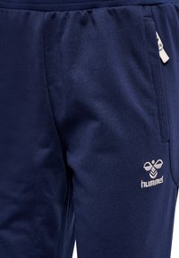 Marineblauwe joggers van zacht materiaal, met een elastische tailleband, zijzakken en een subtiele geborduurde logo in lichtgrijs.