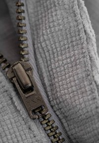 Gray zipper with a textured fabric background. The zipper pull features a dark metallic finish and marked "YKK." Soft, fuzzy texture evident.